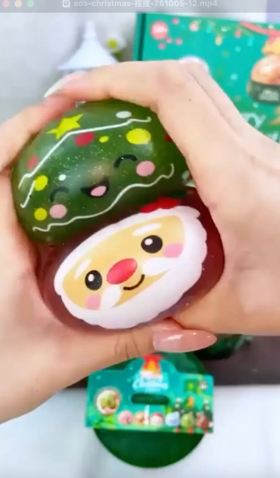Hands demonstrating a festive Christmas squishy toy featuring a decorated green tree and a smiling Santa Claus face. This slow-rising foam stress ball highlights its soft texture and detailed holiday design, perfect for children and collectors.