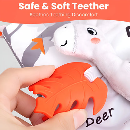 Orange teething toy shaped like a leaf held by a hand, with a white plush toy in the background.