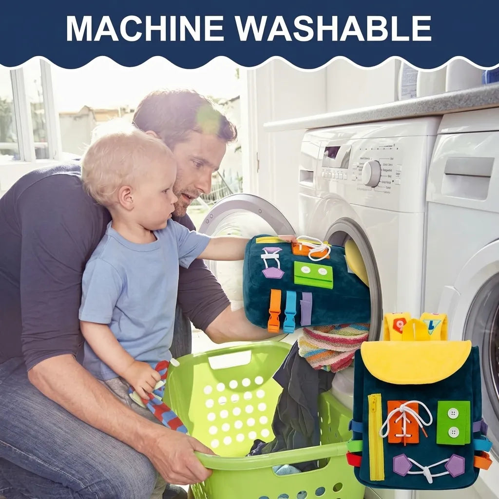 A toddler places a dark teal Montessori busy board backpack into a washing machine. This educational 2-in-1 storage bag features colorful activity panels with zippers, buckles, and buttons for developing fine motor skills.