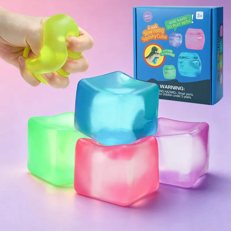 Four colorful translucent slow-rising squishy cubes used as fidget toys for stress relief. A hand demonstrates the soft texture of a lime green cube, accompanied by blue, pink, and purple versions. Retail packaging sits in the background.