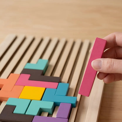 Colorful wooden tangram pieces on a wooden board with a hand holding a pink piece.