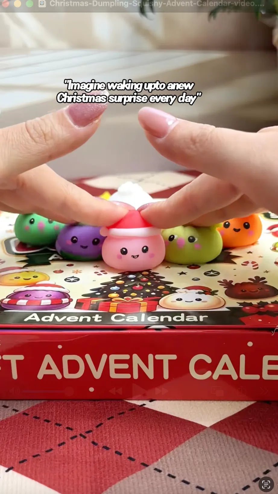 Hands squeezing a pink Santa-hat dumpling squishy from a Christmas advent calendar set. Assorted colorful soft toy dumplings in green, purple, and orange rest on top of the festive holiday-themed box packaging.